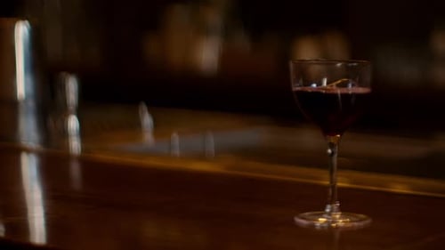 Close-up of cocktail glass on wooden counter, creating a relaxed, sophisticated bar vibe