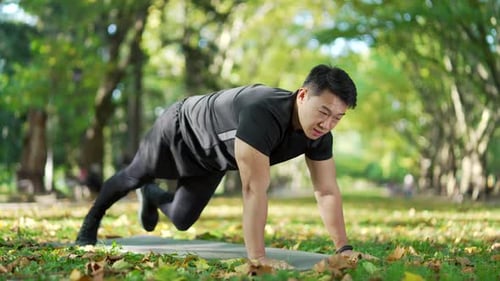 Athletischer asiatischer Mann turnt auf einer Matte in einem städtischen Stadtpark. Ein hübscher Mann in einem Sportanzug