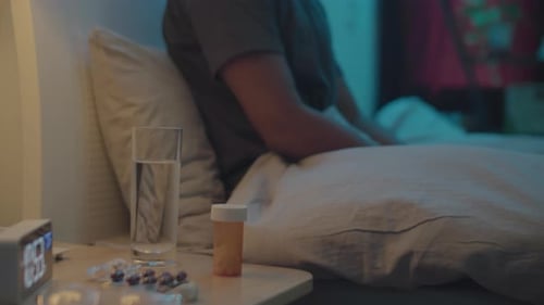 Person Sitting in Bed with Medicine at Night