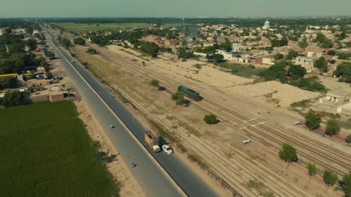 Vista aérea lateral rastreando um trem e carros em uma vila perto de Multan, Punjab, Paquistão