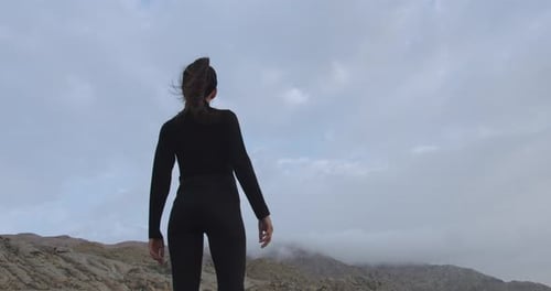 Close-up of a woman in black standing strong in a mysterious desert at sunrise while the wind blows