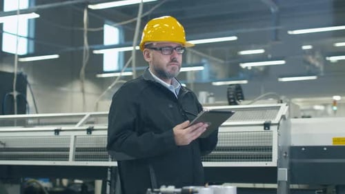Der leitende Ingenieur mit Schutzhelm benutzt einen Tablet-Computer in einer Fabrik.