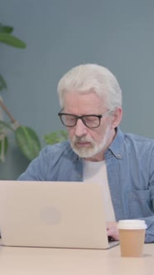 Senior Man Working at Laptop with Coffee Indoors