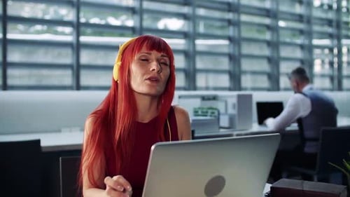 A Mature Woman With Headphones In Office, Listening To Music.