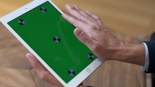A man works at a tablet. A hand in a suit moves along the green screen. Close-up