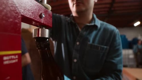 Adult Using Machine To Seal Brown Bottles