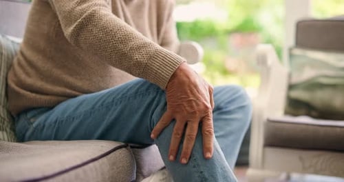 Senior Man Massaging Knee While Sitting Indoors