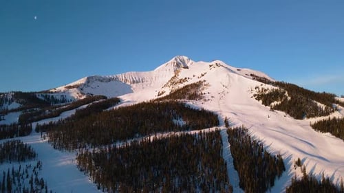 A drone shot of snowy Big Sky, Montana in winter, showcasing the ski resort and majestic mountain te