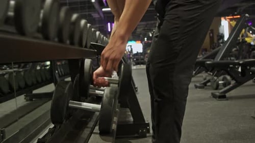 A Muscular Unrecognizable Man Lifts Two Dumbbells Before Beginning His Workout at the Gym