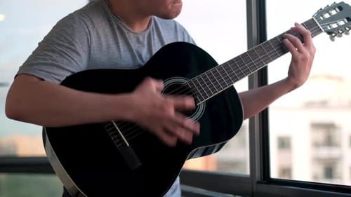 Man Playing Acoustic Guitar by Bright Window at Home