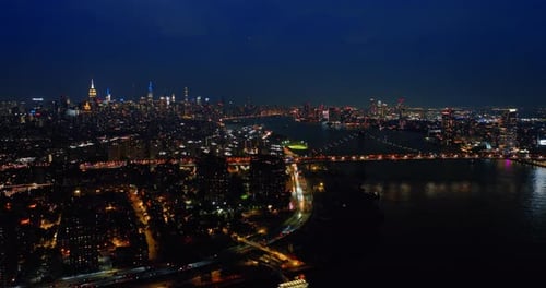 Footage above the dark waters of the East River at night. Luminous cityscape of New York