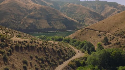 Vehicle drives down dirt road towards river in bottom of large gorge