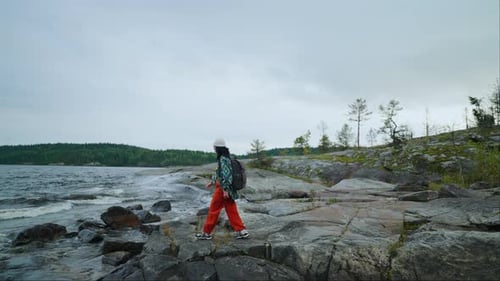 Human And Nature Female Tourist With Backpack Walking On Stone Shore Of Big Lake