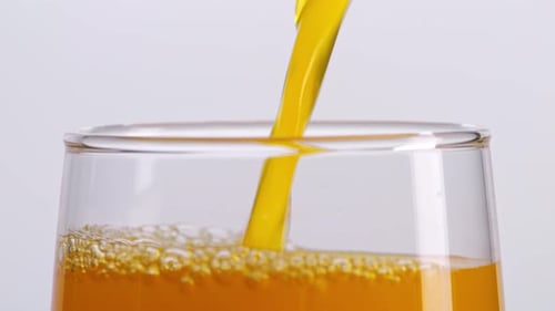 Close Up Of Orange Juice Being Poured Into A Glass On The Light White Screen Background