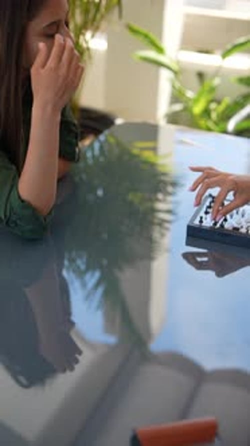 Two Competitors Engaging in a Chess Match on Glass Table with Reflective Surface