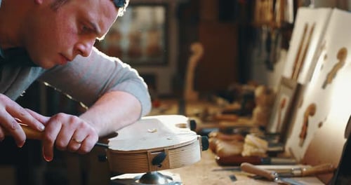Slow motion close up of master artisan luthier painstaking detailed work on wood violin in a works