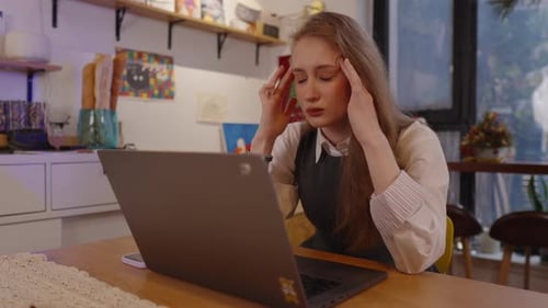 Woman with Headache Massaging Temples at Table with Laptop