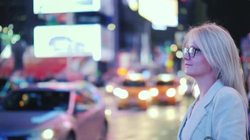 Uma mulher está na Times Square em Nova York. Táxis amarelos reconhecíveis estão passando por um símbolo do