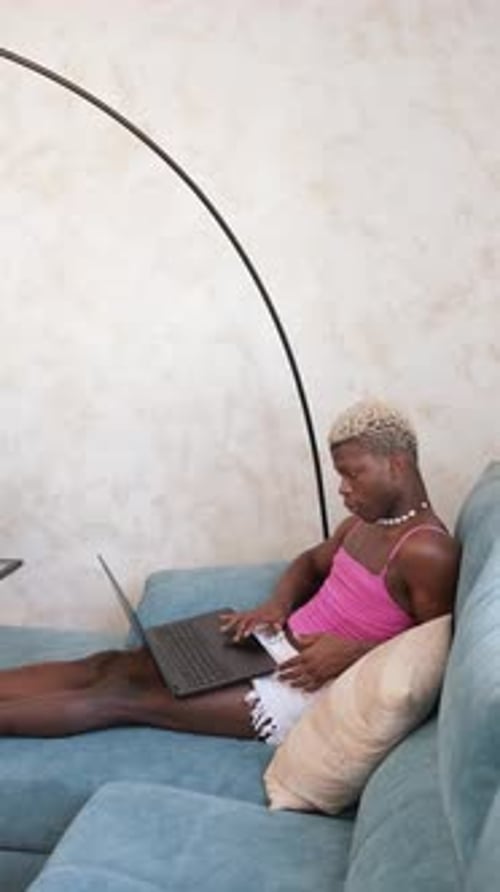 Young Adult Typing on Laptop Lying on Couch