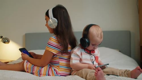 Girl and Infant with Headphones on Bed