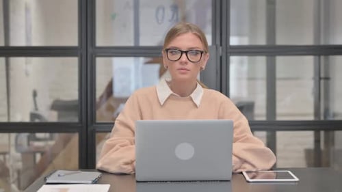 Young Woman Looking at Camera while Working on Laptop in Office