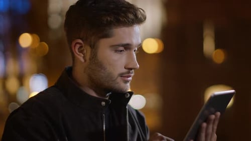 Closeup Serious Guy Scrolling Tablet Computer on Dark City Street. Portrait Of