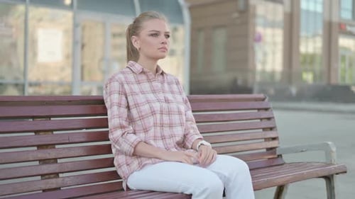 Young Woman Waiting on Bench in City Park