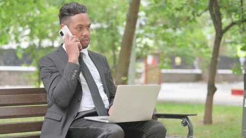 Businessman Works on Laptop and Phone in Park