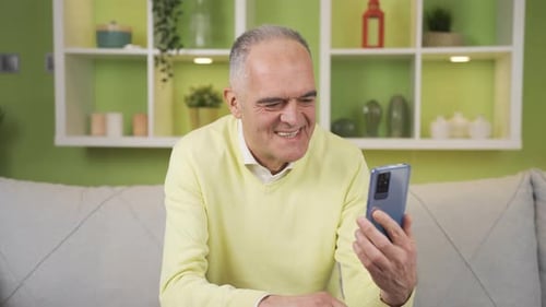 Senior Man Smiling While Using a Smartphone Indoors