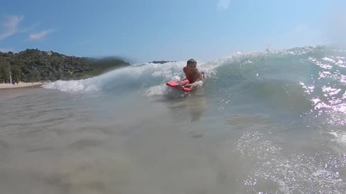 Young man surfer haves fun in the tropical sea and surfs the small wave on the red bodyboard