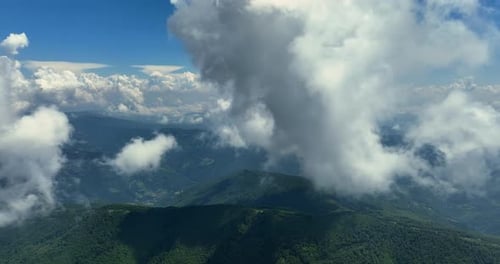 Flying trough white fluffy clouds above green mountain peaks. Beautiful summer sunny day on the high