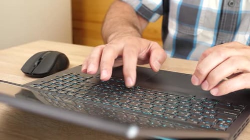 19Close-up of hands using a laptop keyboard and mouse on a wooden desk. Work, internet browsing, and