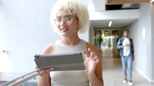 Using tablet, woman walking in modern office hallway, focusing on screen