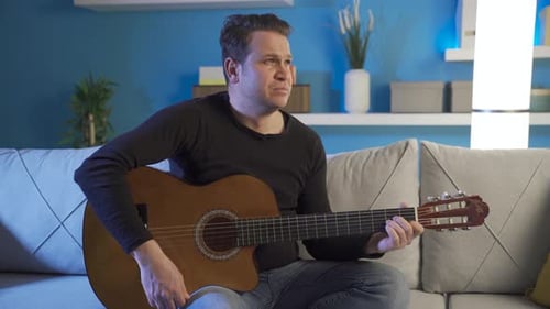 Man Playing Acoustic Guitar Sitting on Couch Indoors