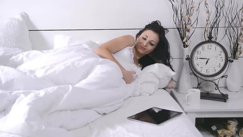 Woman Relaxing in Bed Looking at Tablet