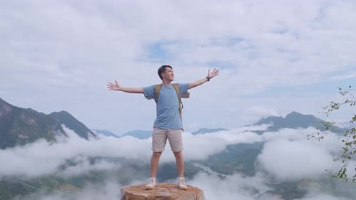 Homem de pé na rocha e levantando as mãos comemorando a chegada ao topo da montanha nebulosa