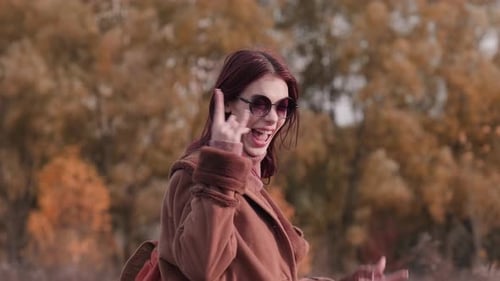 Teen girl wearing sunglasses, making a playful rock gesture and laughing