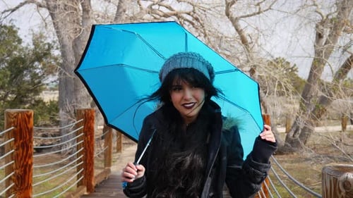 A pretty woman looking cute and smiling with a blue umbrella during a break in the rain storm in slo