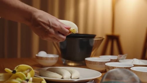 A woman is preparing dessert, she is peeling bananas, bowls with ingredients on the table
