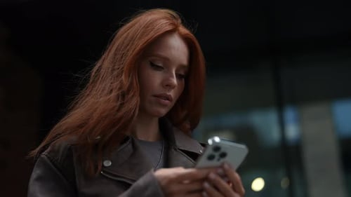 Lowangle View of Cheerful Cute Young Woman Wearing Fashion Leather Jacket Using Typing Mobile Phone