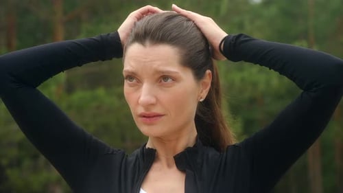 Woman Puts Hair in Ponytail Before Exercising Outdoors