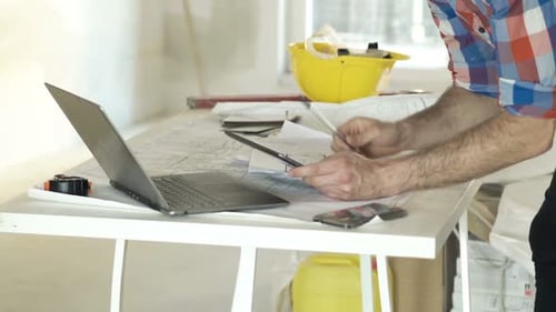 Architect working on blueprints with laptop in home