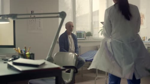 Doctor Consulting Old Man In Hospital Office. Back View Woman Physician Talking With Senior Patie...