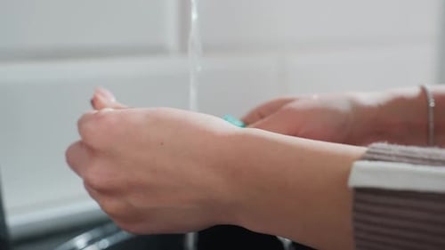 Closeup of Hands Washing Spoon Under Running Tap Water in Modern Kitchen