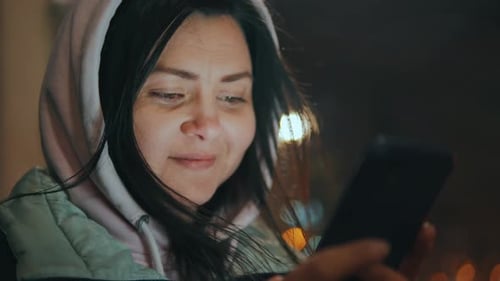Portrait of a Young Woman Texting on Her Smartphone on a City Street at Night