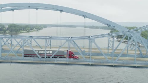 Aerial side view of a semi truck driving on suspension bridge over river