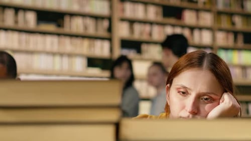 Young Woman Tired of Reading Books From Tall Stack at Quiet Library Table