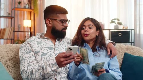 Indian Family Couple Man Woman Planning Expenses with Cash and Smartphone Discussing Shopping Salary