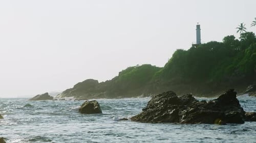 Lighthouse Stands Atop Rocky Elevation Guiding Mariners During Stunning Ocean Sunset Waves Crash