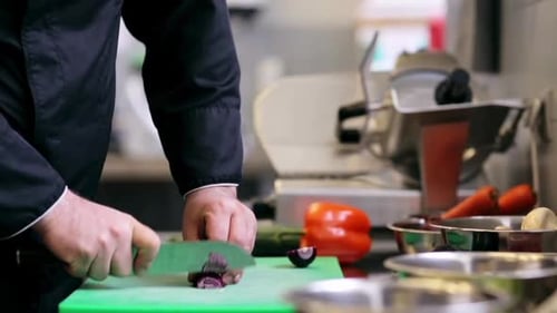 Male chef hands skillfully chopping fresh red onion in restaurant kitchen